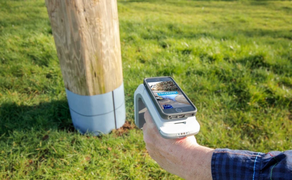 Polesaver RFID Asset Tracking Image Showing Smartphone attached to RFID reader pointed at a wooden utility pole with a polesaver sleeeve on Polesaver RFID Asset Tracking Image Showing Smartphone attached to RFID reader pointed at a wooden utility pole with a polesaver sleeve on
